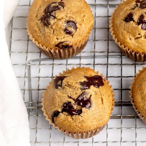 Closeup of moist banana oatmeal muffins on a cooling rack, studded with melty dark chocolate puddles
