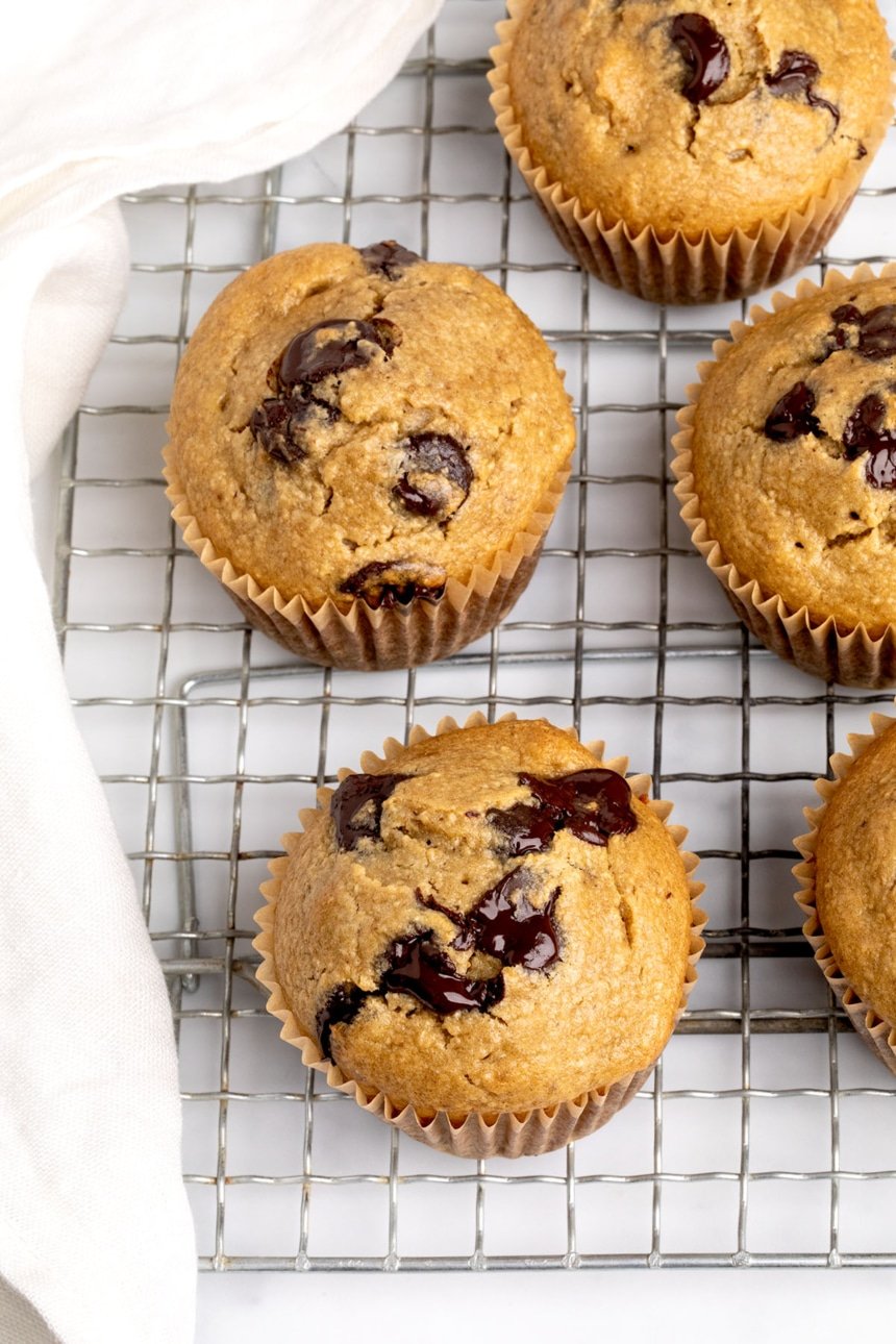 Overhead view of several freshly baked muffins with cracked tops and melty chocolate, on a wire rack