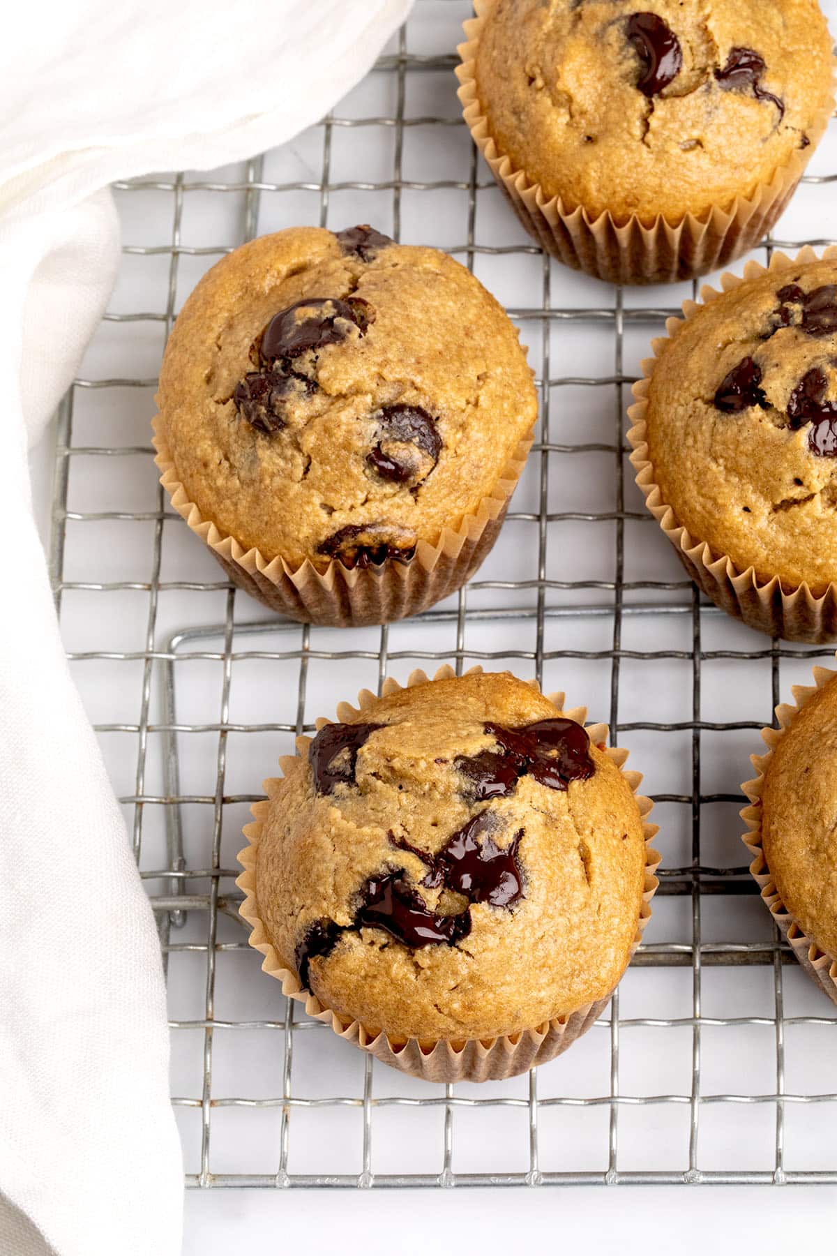 Overhead view of several freshly baked muffins with cracked tops and melty chocolate, on a wire rack