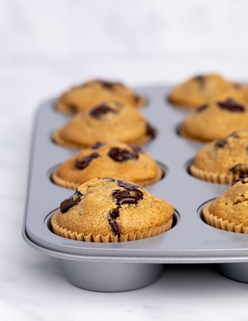 Side view of golden brown muffins still in the pan, with domed tops and pockets of melted chocolate