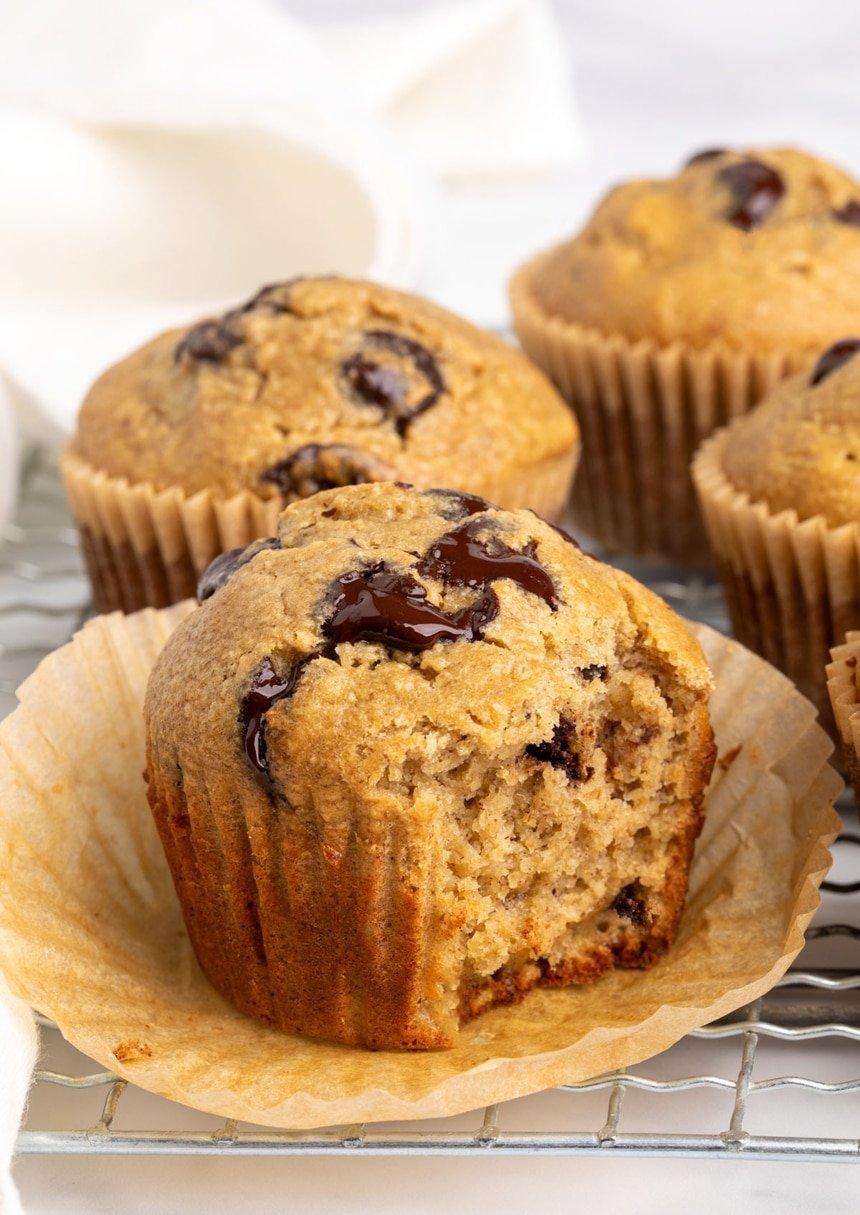 One muffin with the wrapper peeled back and a bite taken, showing its soft, tender interior with gooey chocolate