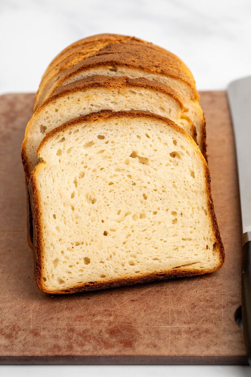 slices of tall gluten free bread made with psyllium husk with soft crumb and brown crust on brown cutting board with large bread knife