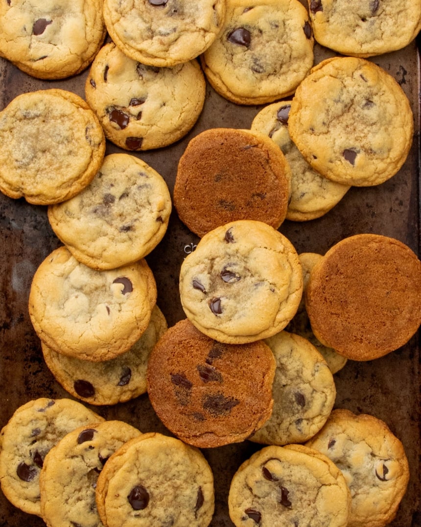 scattered light brown gluten free chocolate chip cookies with golden edges on dark brown baking sheet, made with xanthan gum substitutes