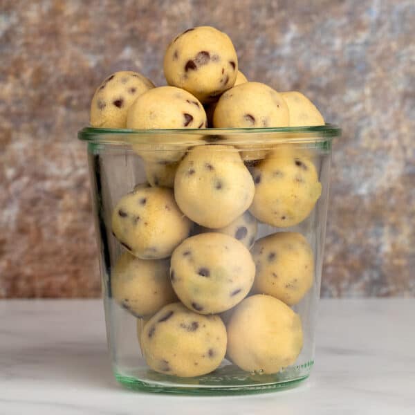 Glass jar filled with neatly rolled balls of gluten free cookie dough, ready for snacking