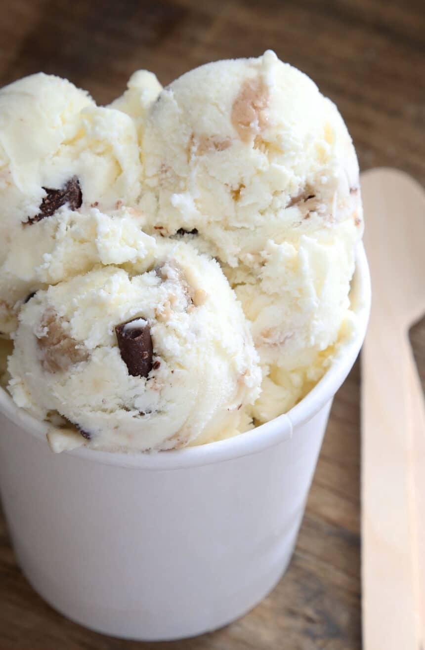 Vanilla ice cream in scoops with brown cookie dough bites and chocolate pieces in white pint container