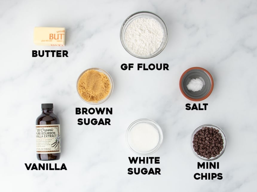 Overhead view of labeled ingredients for edible cookie dough, including butter, sugars, gluten free flour, vanilla, salt, and mini chips.