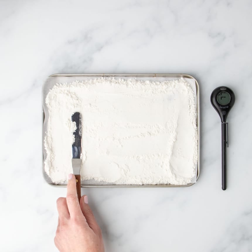 Spreading flour on a baking sheet for heat treatment, with a digital thermometer nearby to ensure safety