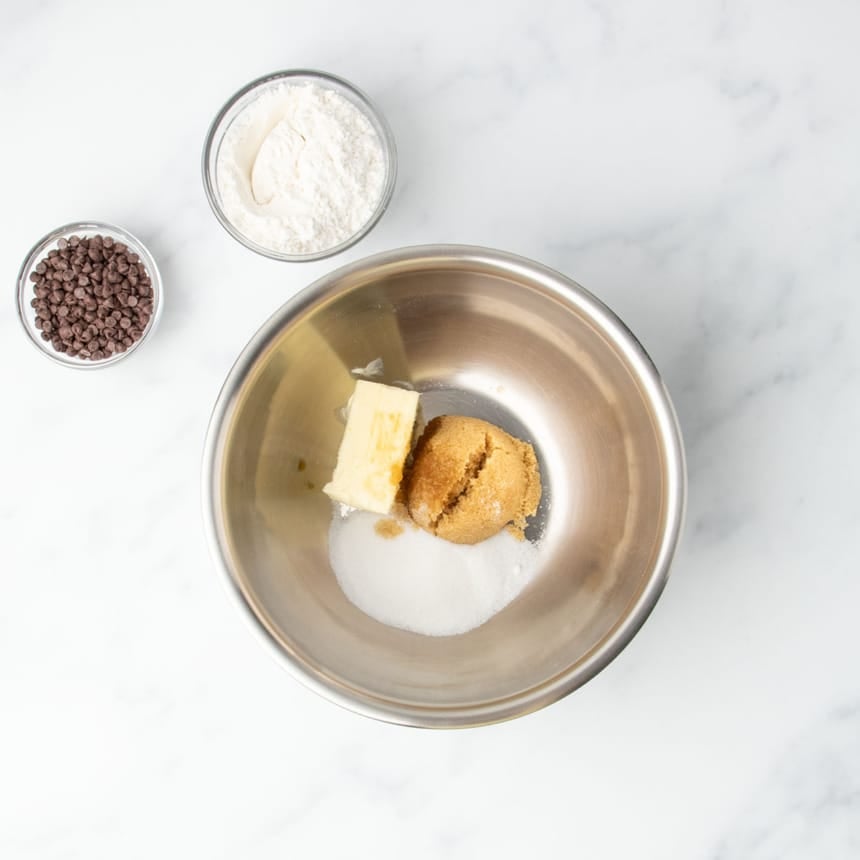 Brown and white sugars with butter in a metal mixing bowl, ready to be mixed for cookie dough