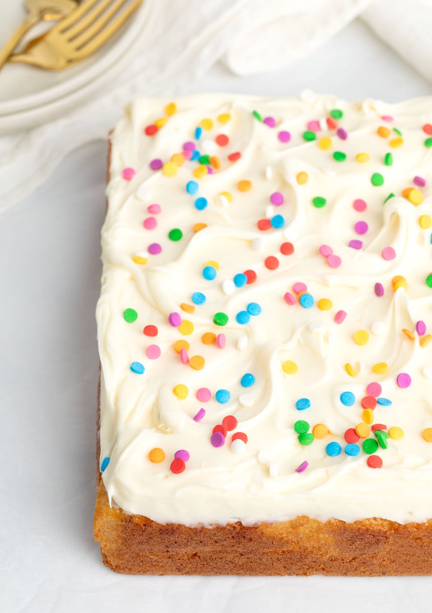 Celebration-ready square yellow cake topped with white frosting and multi-colored edible confetti sprinkles.