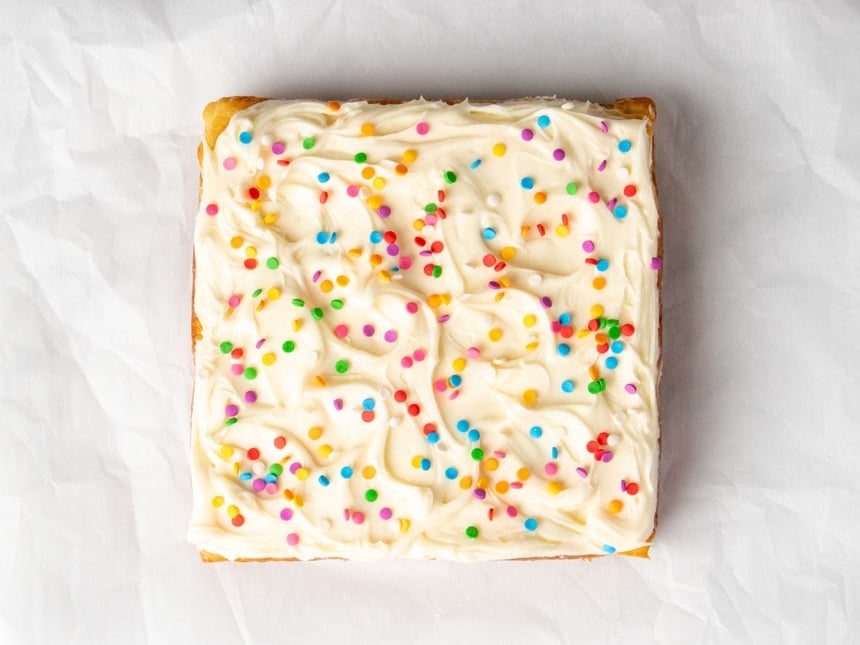 Top-down view of the full gluten free dairy free vanilla cake on parchment, decorated with swirled white dairy free frosting and colorful round sprinkles.