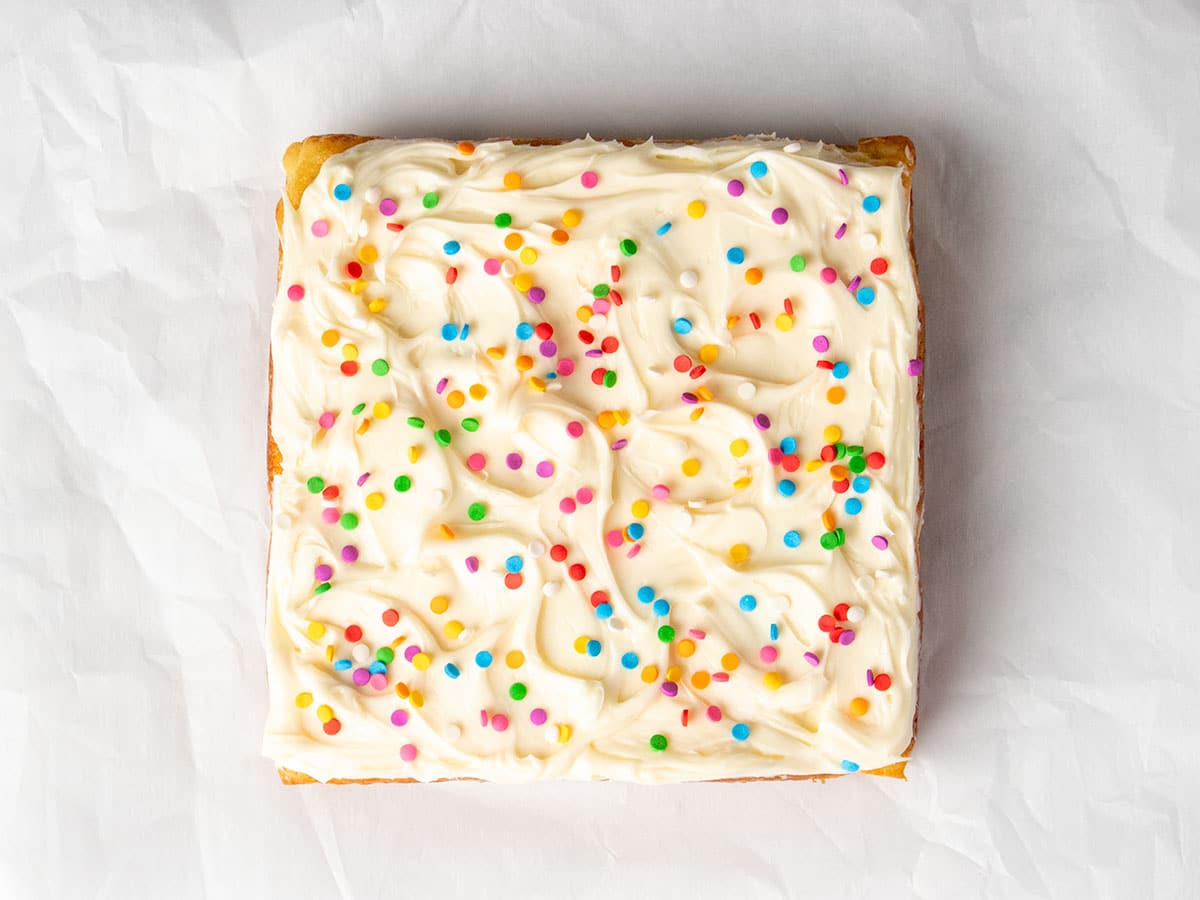 Top-down view of the full gluten free dairy free vanilla cake on parchment, decorated with swirled white dairy free frosting and colorful round sprinkles.