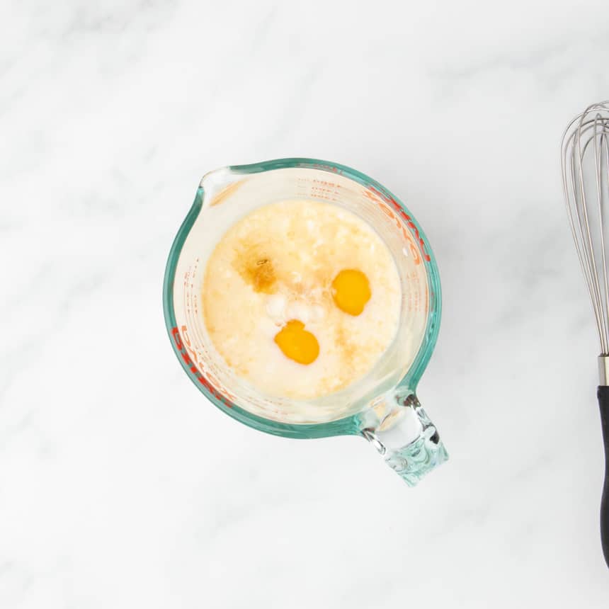 Glass measuring cup filled with dairy free milk, eggs, dairy free yogurt, and flavorings like vanilla extract before mixing.
