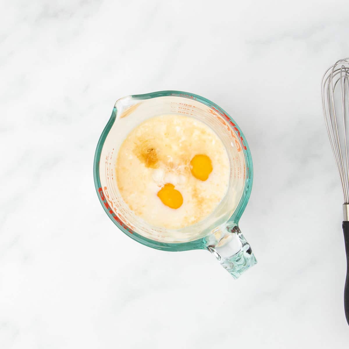 Glass measuring cup filled with dairy free milk, eggs, dairy free yogurt, and flavorings like vanilla extract before mixing.