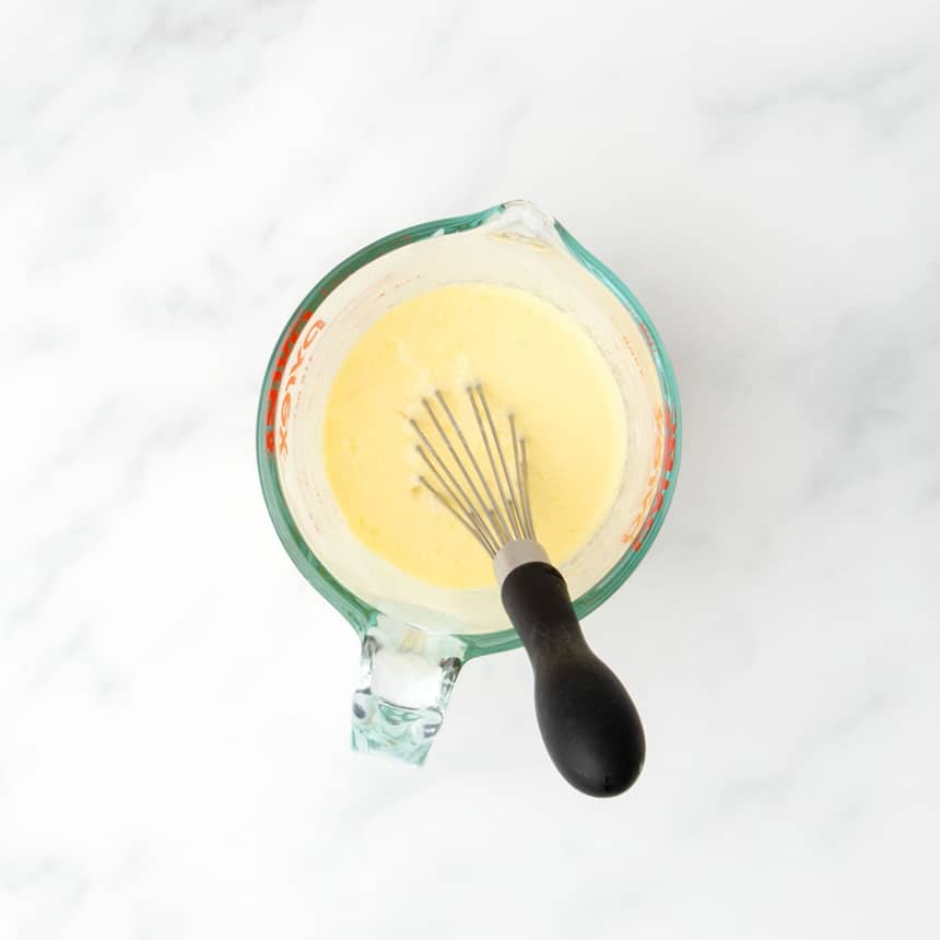 Wet ingredients whisked together in a glass measuring cup to form a smooth, pale yellow mixture.