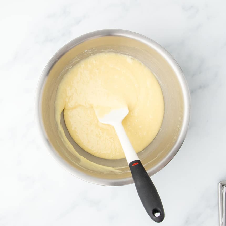 Gluten free cake batter fully mixed and smooth in a large stainless steel mixing bowl with a white silicone spatula.