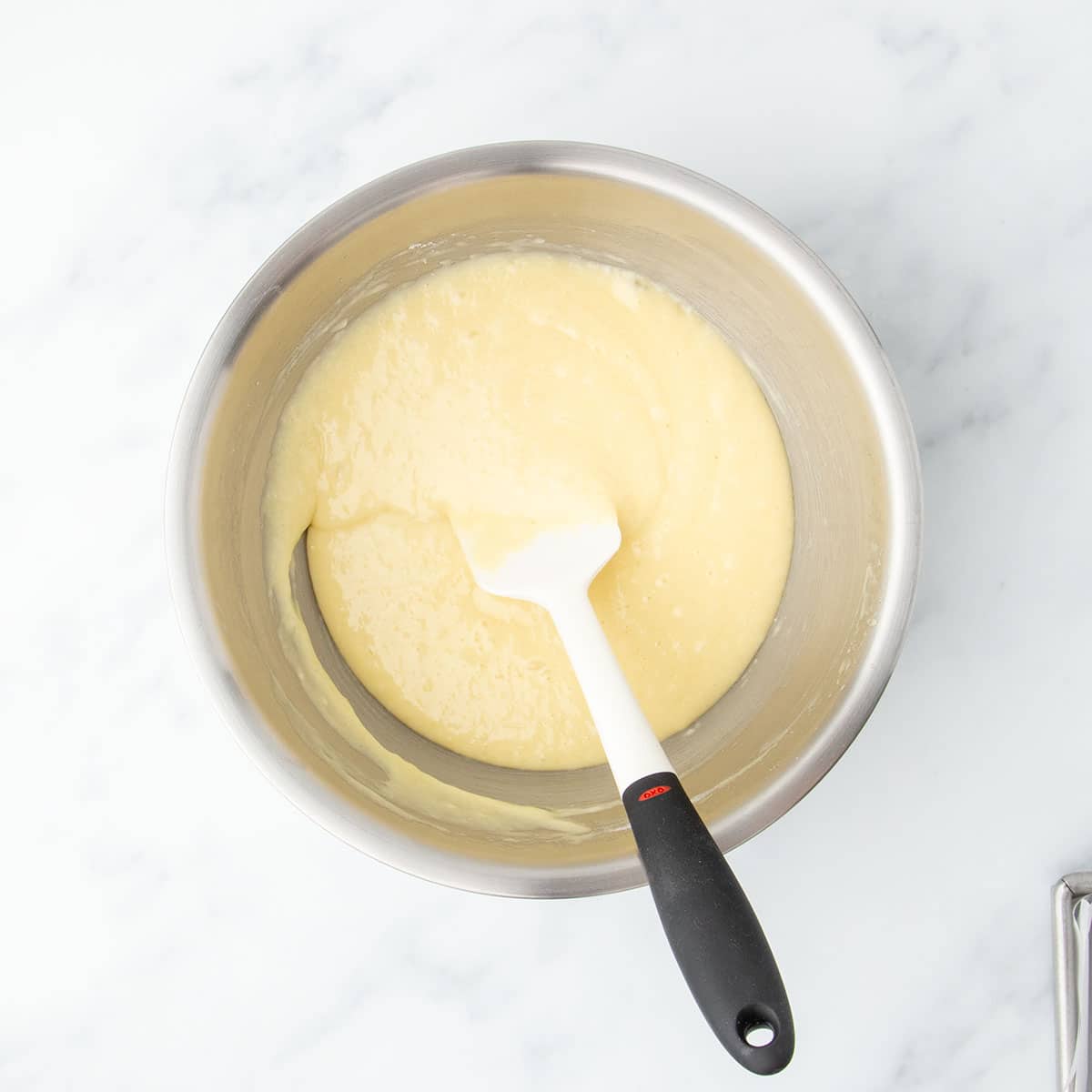 Gluten free cake batter fully mixed and smooth in a large stainless steel mixing bowl with a white silicone spatula.
