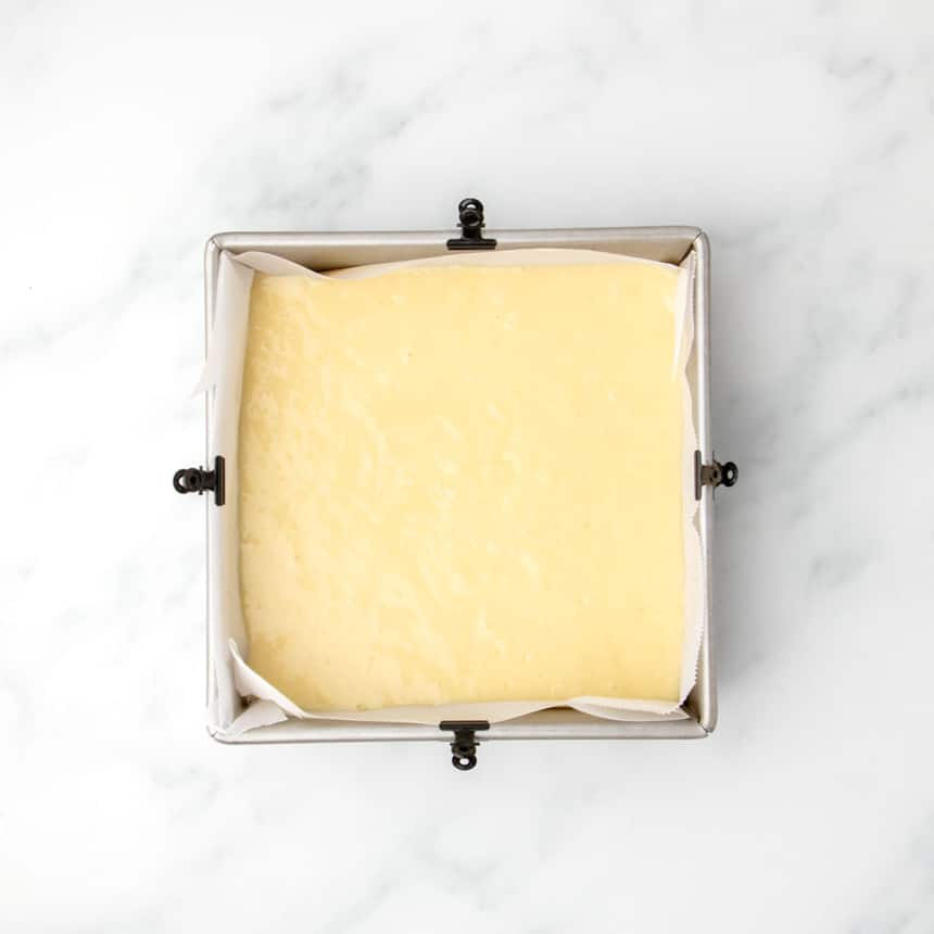 Prepared cake batter evenly spread in a parchment-lined square baking pan, ready for the oven.