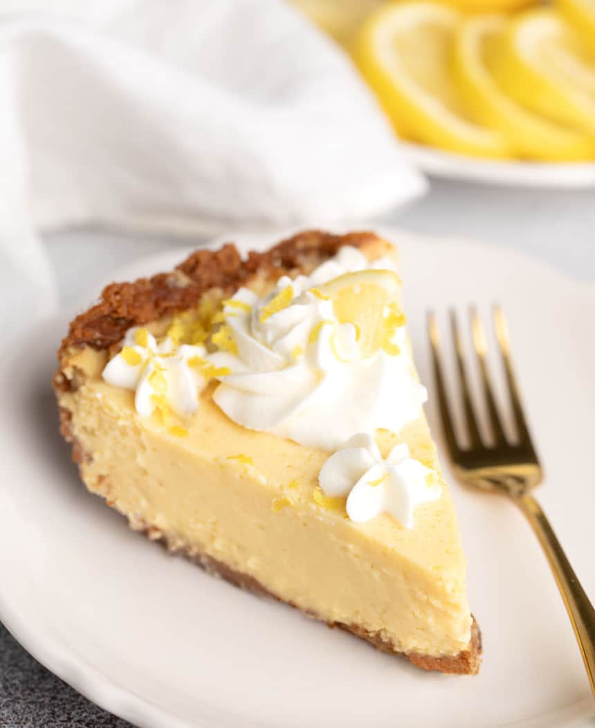 Slice of chilled lemon pie topped with whipped cream and lemon zest, served with a gold fork