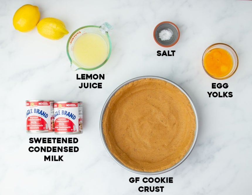 Labeled ingredients laid out for lemon pie, including lemon juice, sweetened condensed milk, egg yolks, salt, and a gluten free cookie crust