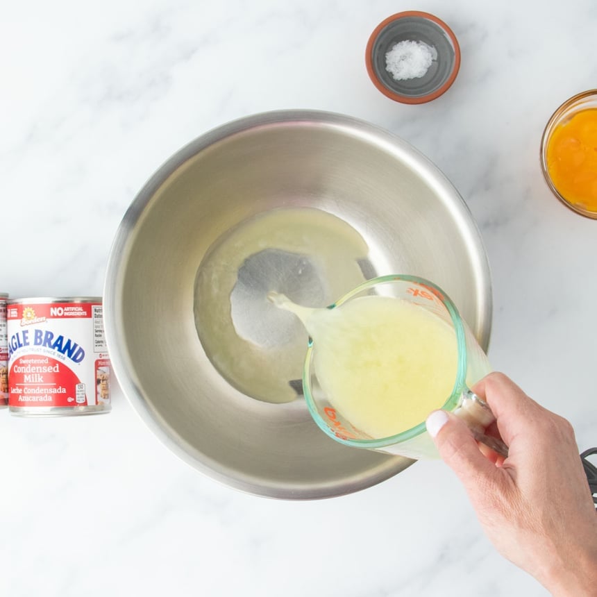 Lemon juice being poured into a large mixing bowl, surrounded by other ingredients on a marble surface.