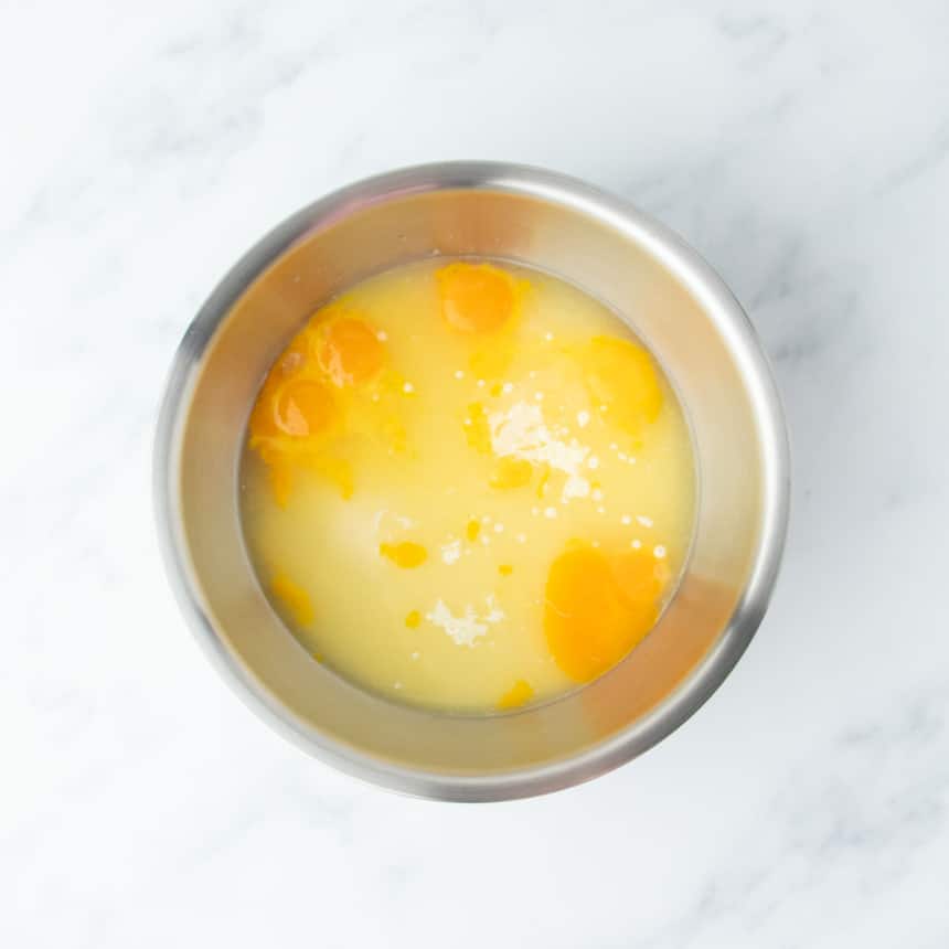 Top-down view of egg yolks and lemon juice added to the bowl with sweetened condensed milk.
