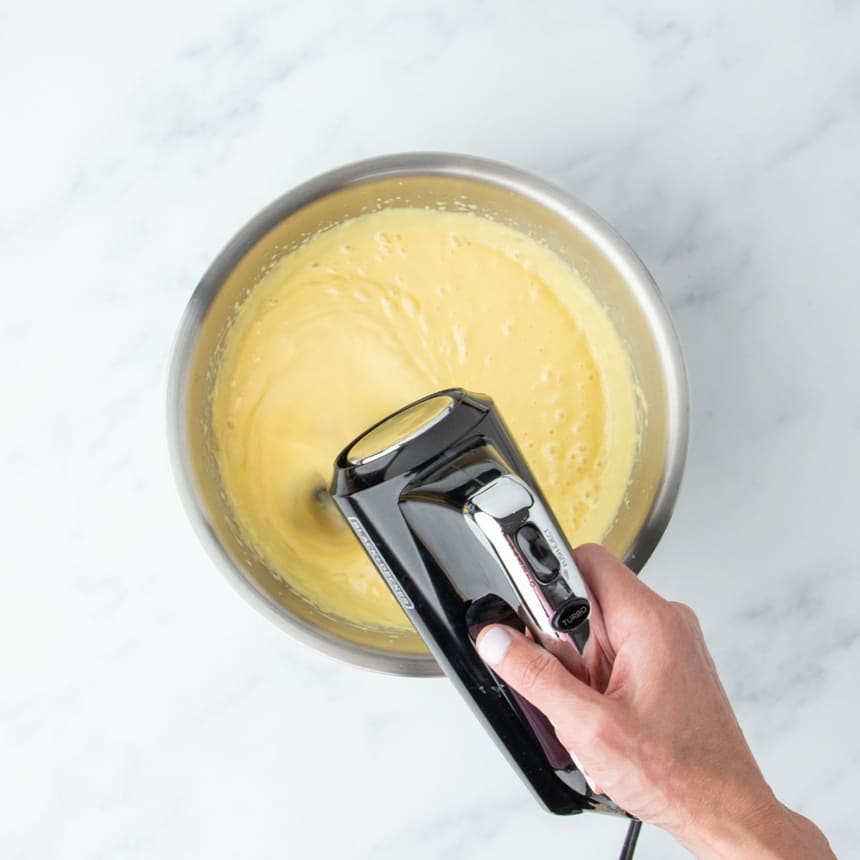 Hand mixer whipping the lemon pie filling in a metal bowl until smooth and creamy.
