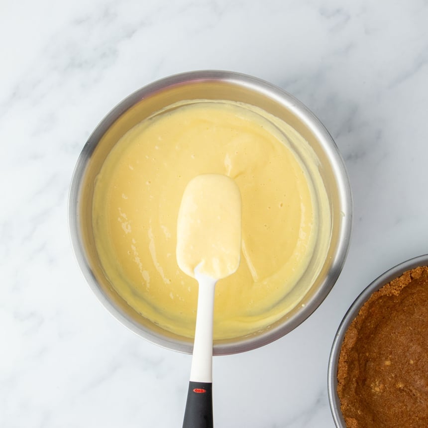 Spatula resting in a bowl of smooth lemon filling, ready to be poured into the crust