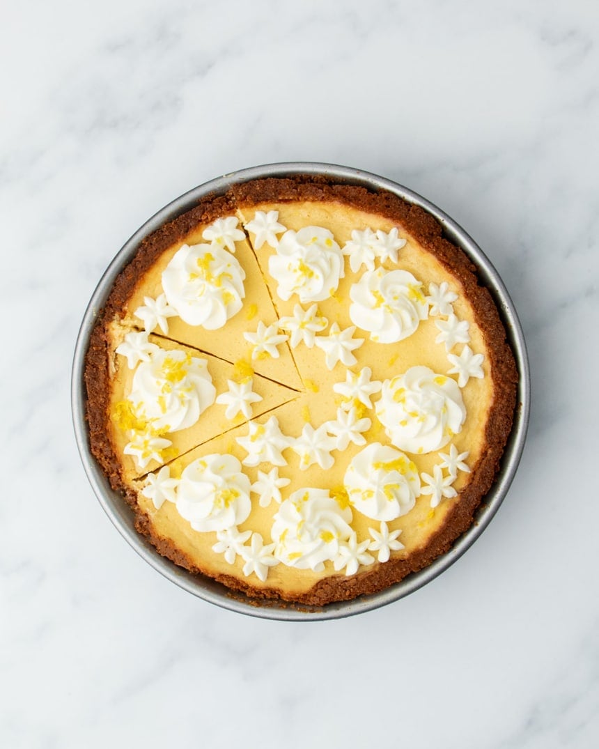Fully baked lemon pie decorated with piped whipped cream and lemon zest, with a few slices cut but not removed.
