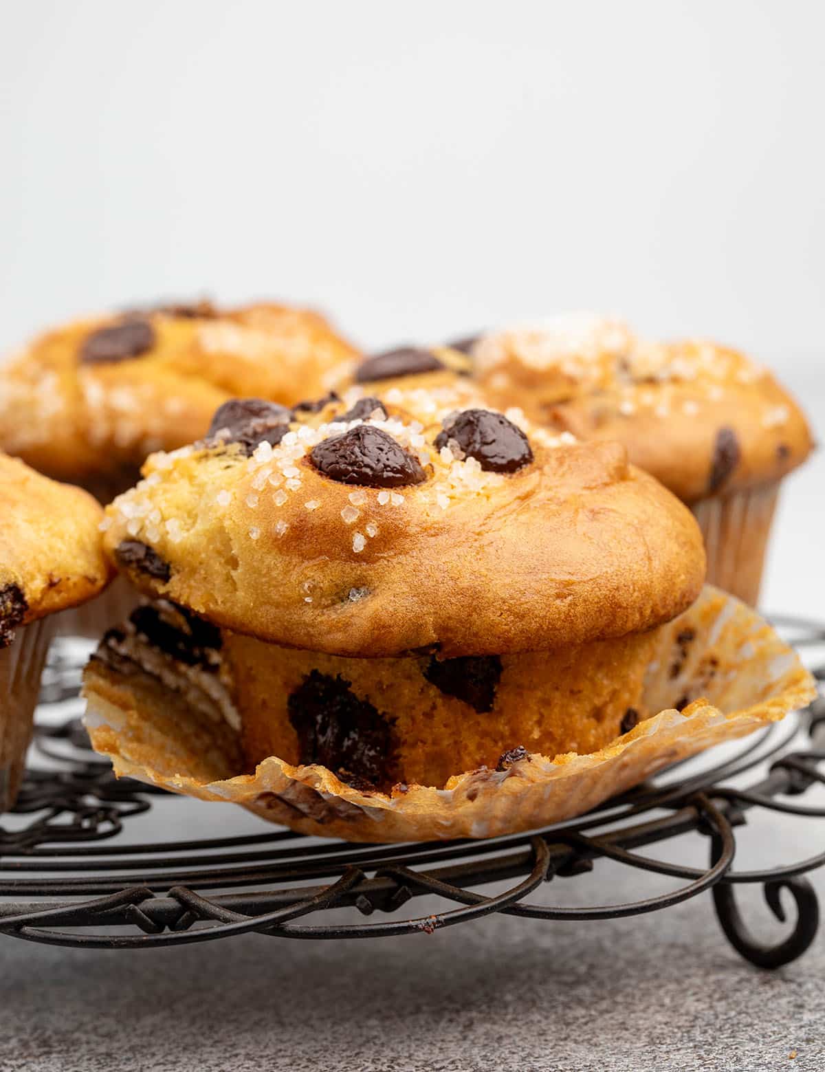 Close-up of a chocolate chip muffin on a cooling rack, wrapper peeled back to show the tender crumb