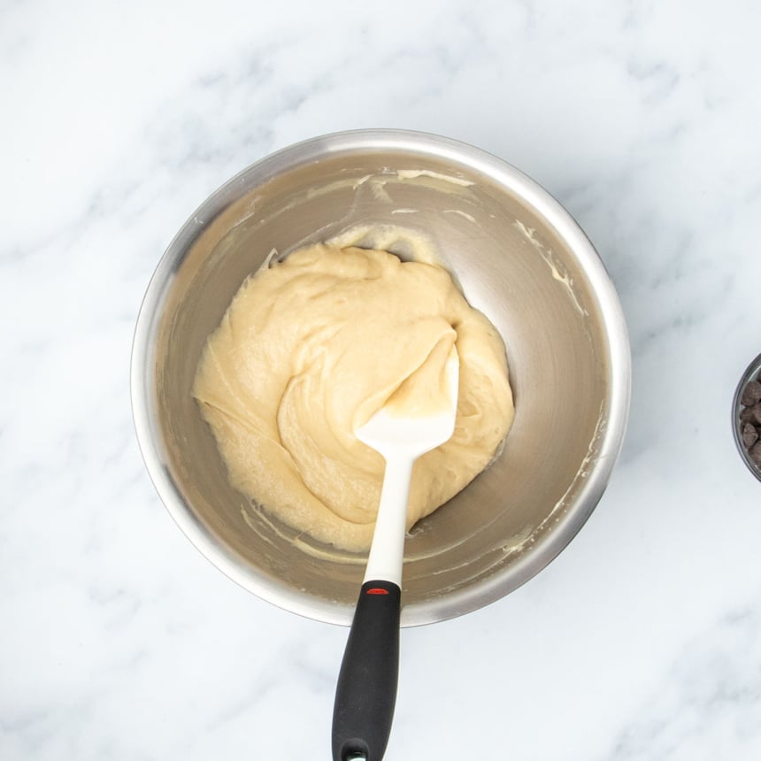 Thicker muffin batter after having rested being turned over with a silicone spatula before folding in chocolate chips.
