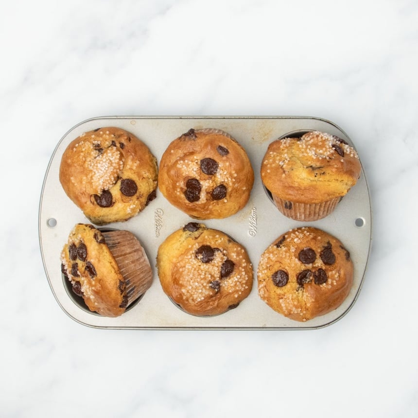 Freshly baked gluten free vegan muffins in the tin, golden brown with chocolate chips and sugar on top.