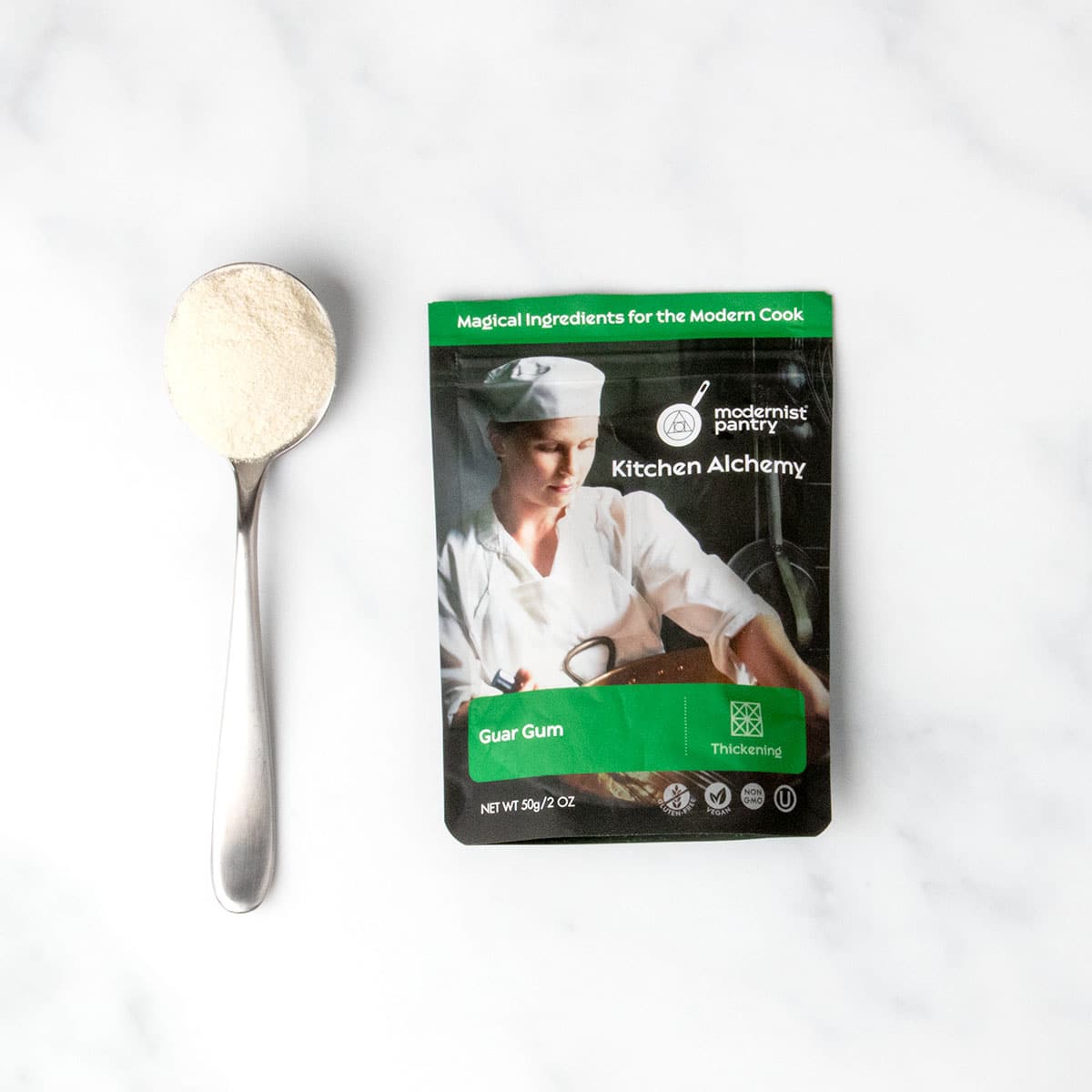 black and green pouch of guar gum with sample of white powder on large metal spoon