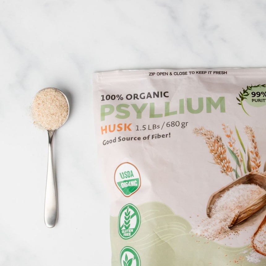 light brown and green package of whole psyllium husk with sample of light brown dry flakes on large metal spoon