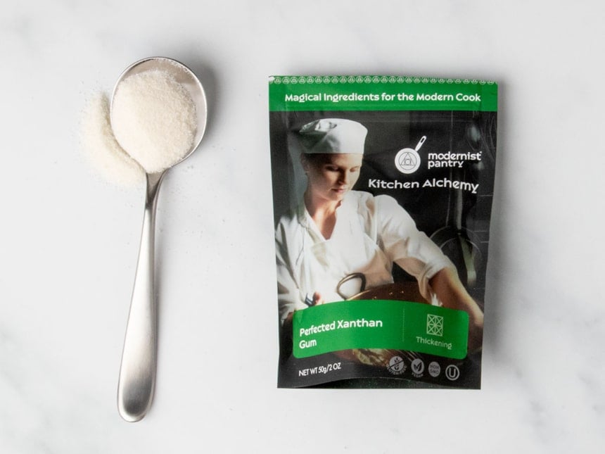 black and green pouch of xanthan gum with sample of white powder on large metal spoon