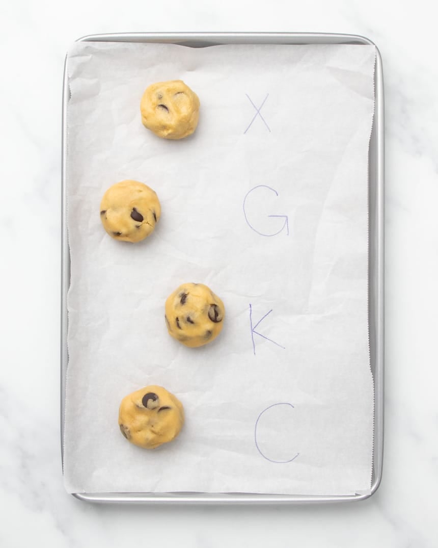 4 raw round disks of gluten free chocolate chip cookies dough on white parchment paper with the letters written next to each indicating which xanthan gum substitute they were made with