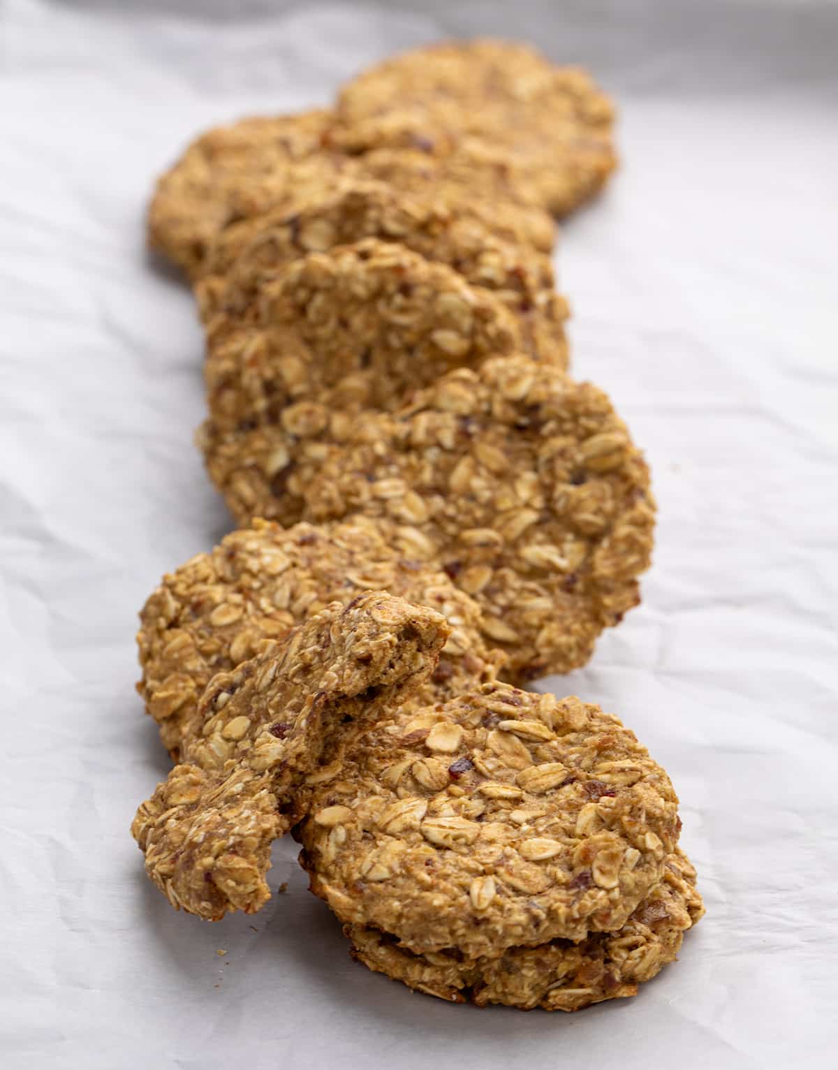 9 whole grain round light brown cookies in a row, one with a bite taken, on white paper