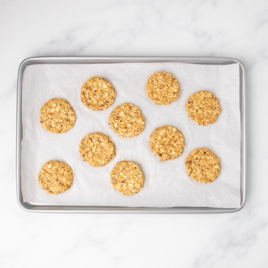 10 evenly spaced round raw cookie disks on white paper on baking tray