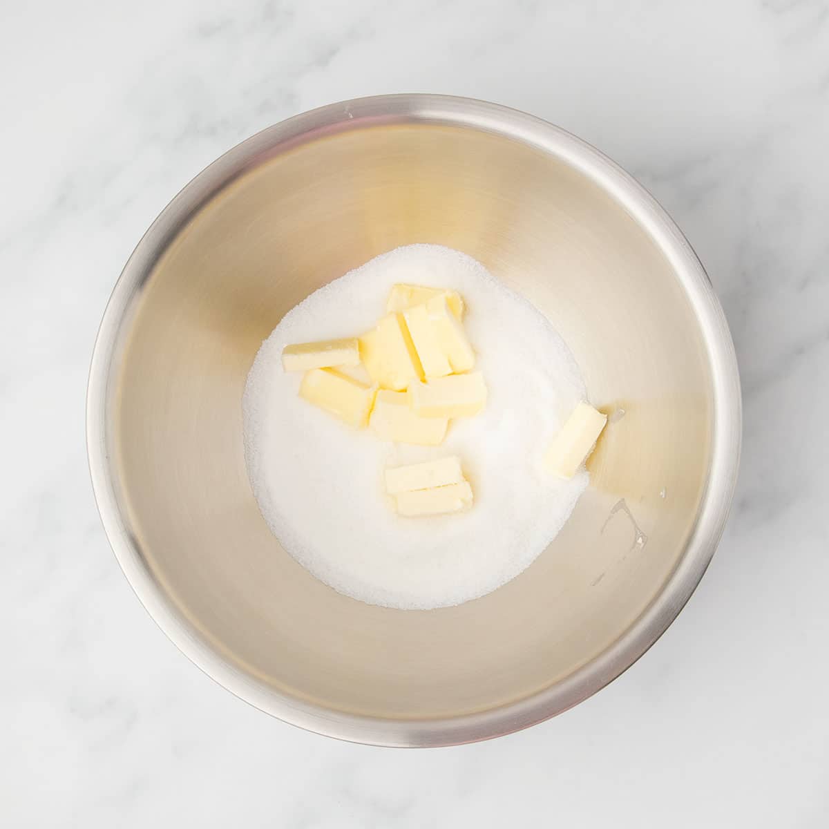 Softened butter and granulated sugar in a large metal mixing bowl, ready to cream
