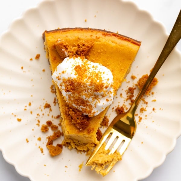 A close-up overhead photo of a slice of spiced orange cheesecake topped with whipped cream and crumbles on a dessert plate.