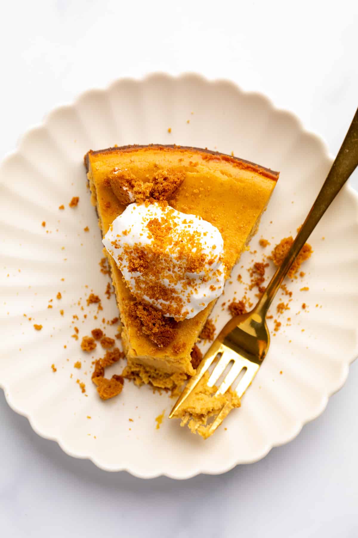 A rich slice of pumpkin spice cheesecake on a scalloped plate with a bite taken out by a golden fork.