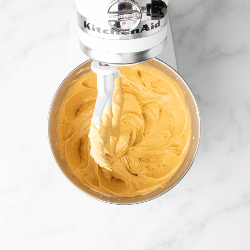Cream cheese filling with added pumpkin puree, pumpkin spice, and vanilla making it orange colored, being mixed until smooth in a stand mixer bowl.