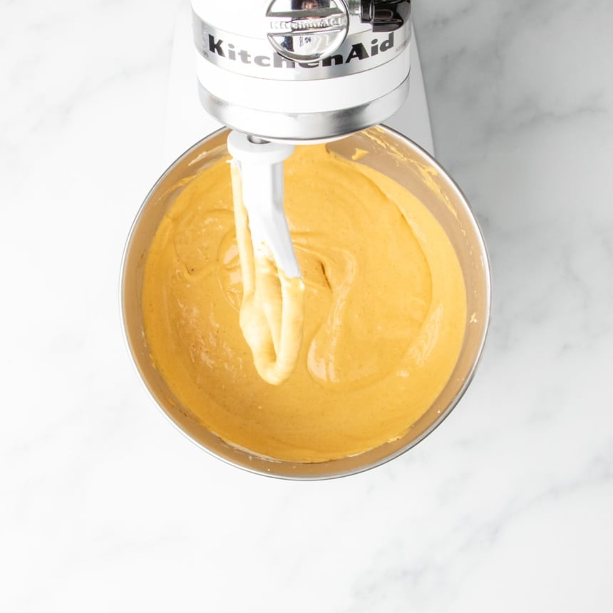 A close-up of the finished, smooth pumpkin cheesecake batter, with eggs beaten in for a somewhat thinner batter, in a stainless steel mixing bowl with the paddle attachment.