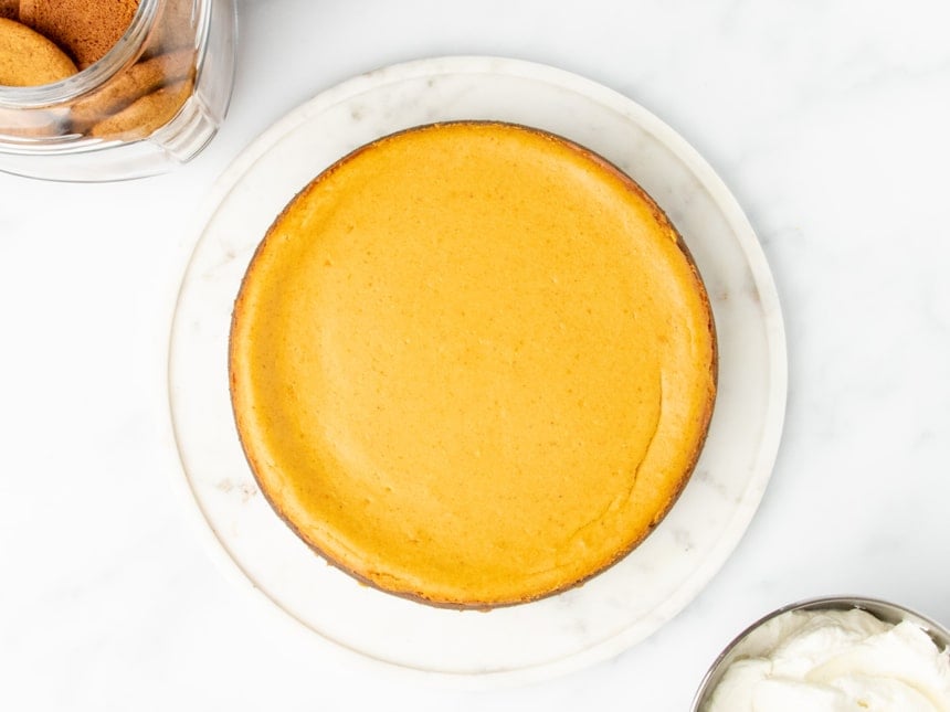 An overhead view of the perfectly baked gluten free pumpkin cheesecake, golden and smooth, cooling on a round marble platter.