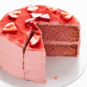 Two-layer pink frosted cake with two slices removed, topped with red powder and fresh strawberry slices.