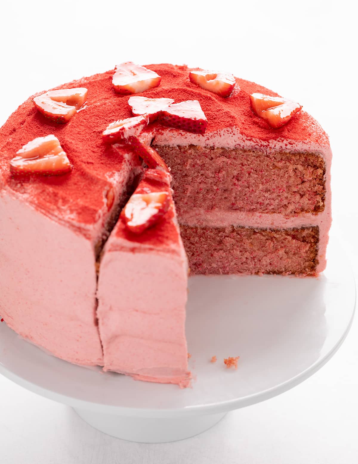 Whole pink frosted cake with two slices cut out, showing the moist interior with visible strawberry flecks.