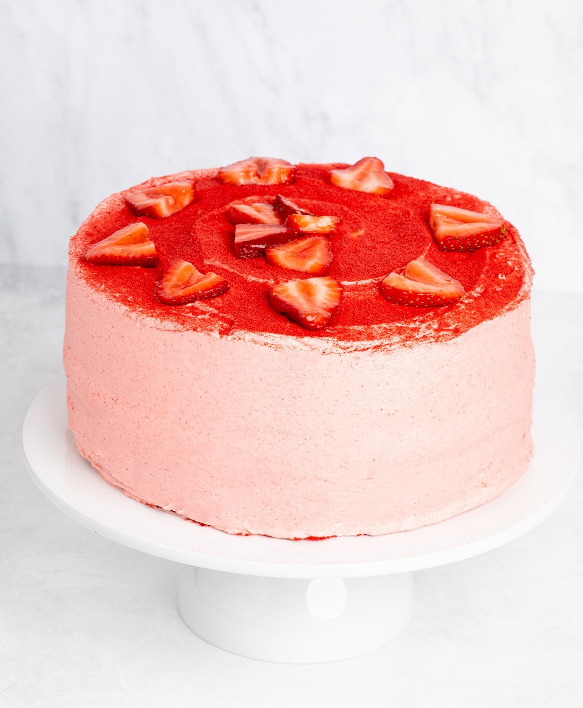 Whole cake covered in pink frosting and red powder, decorated with strawberry slices on top.