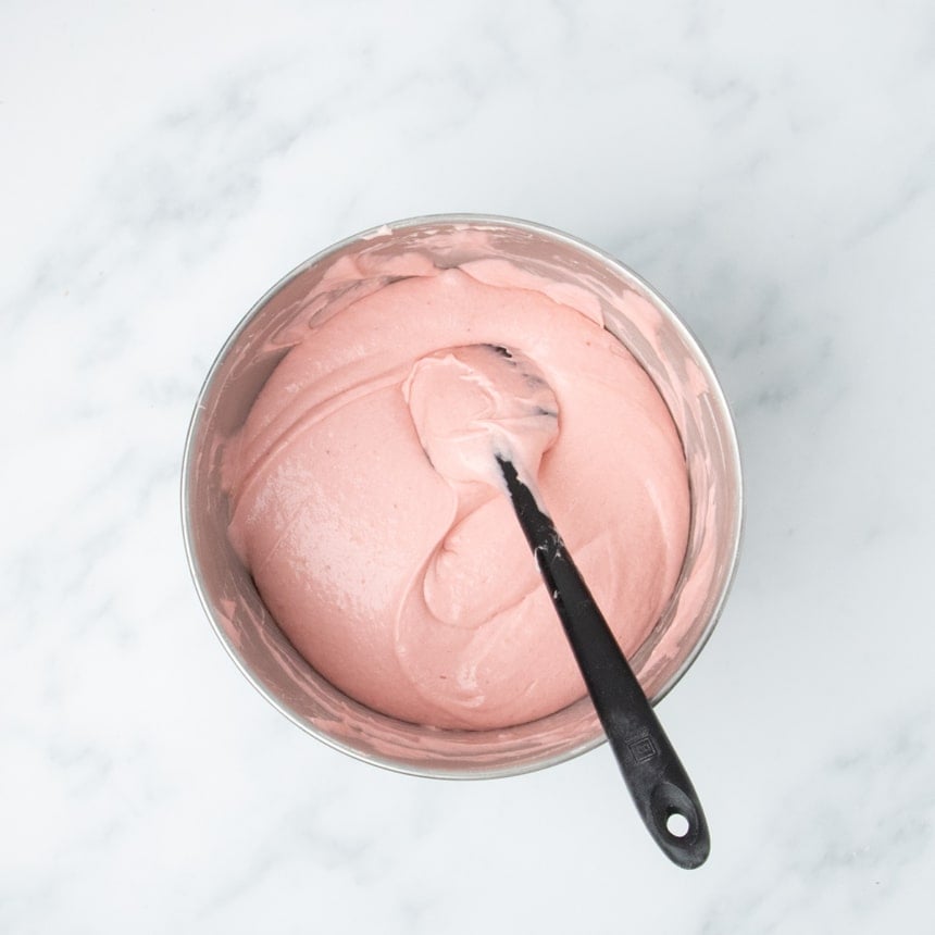 Mixing bowl filled with smooth, pale pink cake batter and a black spatula resting inside.