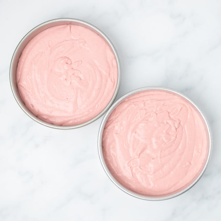 Two round cake pans filled with pink batter, ready for baking.