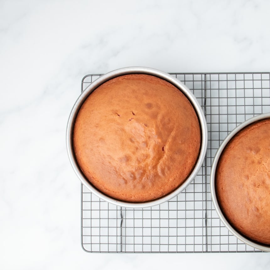 Baked cake layers in pans cooling on a wire rack.