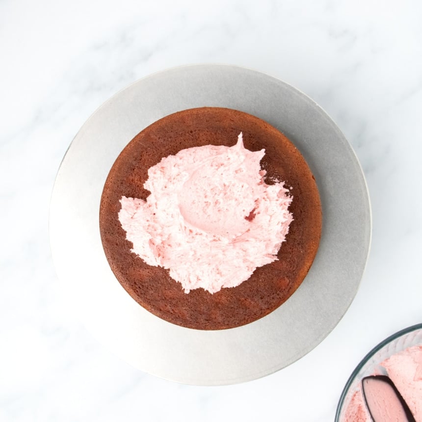 Single cake layer topped with a mound of pink frosting on a round metal turntable